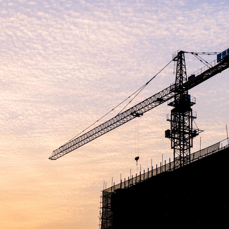 Silhouette of sunset scene with tower crane on the construction site building in city.